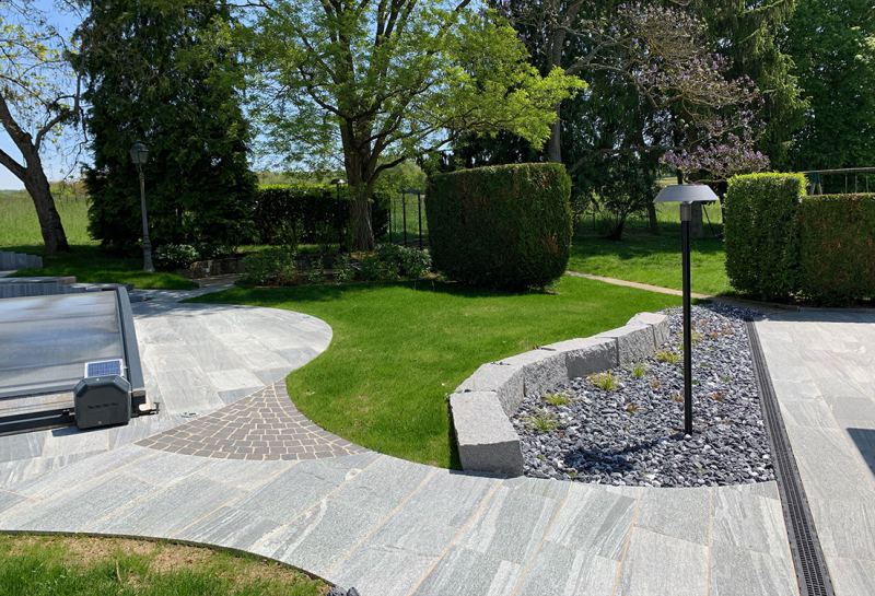 Jardin avec cheminement en dalles de pierre et massif de galets autour d'une piscine
